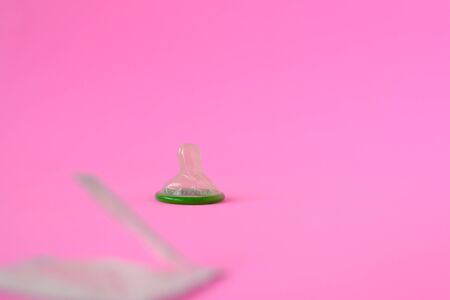 Green condom on pink paper background with copy space for text. Reproductive health and safe sex...