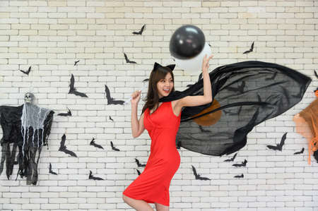 Portrait of beautiful young asian woman wearing witch costume posing with balloons on background decorated for party concept - Free space for copy textの写真素材