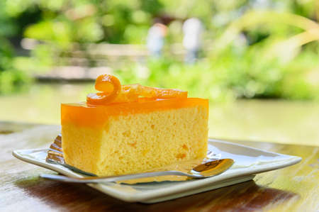Piece of orange cake with fresh orange slice on top and spoon on white dishの写真素材