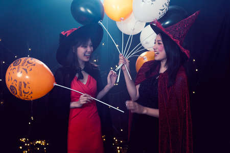 Portrait of two beautiful young woman in witch halloween costumes at party over dark magic...