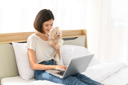 Beautiful young asian woman working on bed in bedroom at home with her maltese dog, Cheerful and...