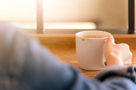 Back view of female hands holding a coffee cup in modern coffee shop, woman drinking coffee during recreation timeの写真素材