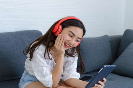 Portrait of beautiful young Asian woman wearing headphones to listening music while relaxing on sofa...