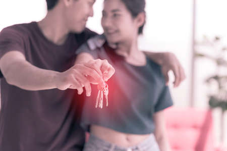 Happy young asian married couple holding key while relocation into new home on moving day, celebrating moving to new home conceptの写真素材