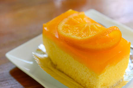 Top view of orange cake with fresh orange slice on top and spoon on white dish with copy space