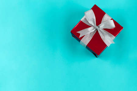 Top view of gift box wrapped in red paper with ribbon on blue colour background. Copy space for text. Holiday concept. Time gifts.の写真素材
