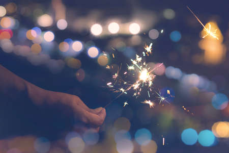 Female hands holding sparkler on bokeh background. Glittering burning sparkler for celebration christmas,festival party backgroundの写真素材
