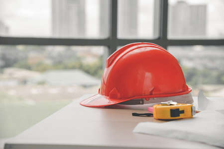 Red hard safety helmet hat, yellow tape measure (measuring tape) and blueprint on table in office worker conference site with copy space. Engineering tools conceptの写真素材