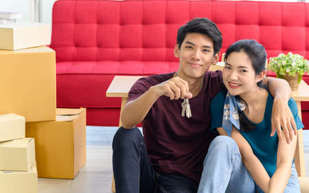Happy young asian married couple holding key while relocation into new home on moving day,...
