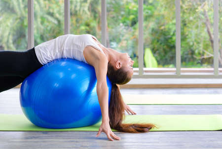 Caucasian woman exercising with exercise ball. Fitness girls flexing abdominal muscles with fit ball in gym roomの写真素材
