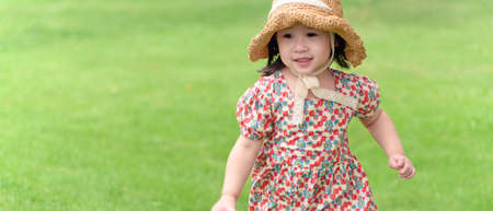 Happy Asian child girl with straw hat and smiling cute face running on meadowの写真素材