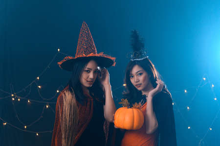 Portrait of two beautiful young woman in witch halloween costumes at party over dark magic background - Halloween party conceptの写真素材