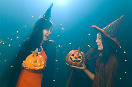 Portrait of two beautiful young woman in witch halloween costumes holding halloween pumpkin Jack O...