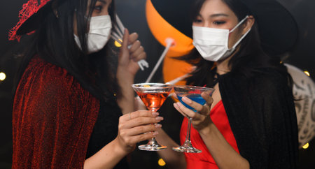 Two beautiful young woman in witch halloween costumes drinking cocktail and holding balloons wearing...