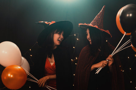 Portrait of two beautiful young woman in witch halloween costumes holding balloons in party over dark magic background - Halloween party conceptの写真素材
