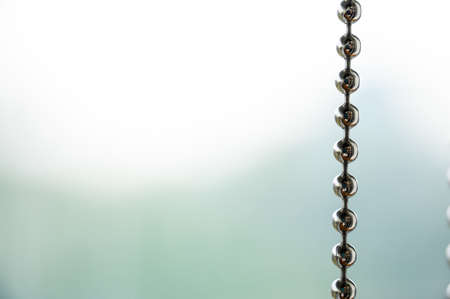 Close up a metal chain of a roller blind with blurred background for copy spaceの写真素材