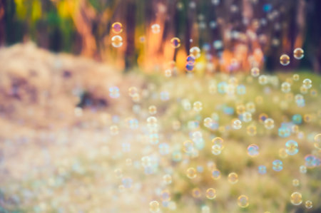 Abstract blurred of rainbow soap bubbles from the bubble blower flying on green grass. spring or summer season background. symbol of childhood. bokeh backgroundの写真素材