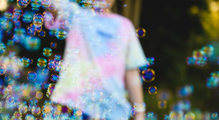 Happy little boy standing and blowing soap bubbles on the outdoor field in summertime