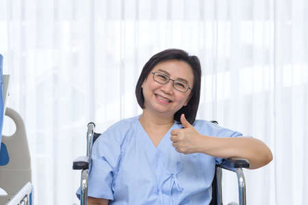 Portrait of senior patient smiling and showing thumbs up while her sit in wheelchair after condition has improvedの写真素材