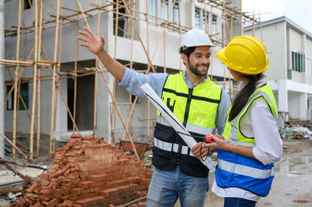 Young attractive construction man and woman in vests with helmets working on the under-construction...