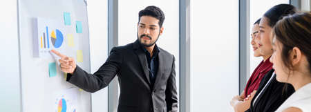 Businessman pointing towards graph and giving Flipchart presentation explaining the idea to diverse partners in the office. Banner cover design of business people meetingの写真素材