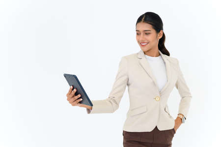 portrait of cheerful attractive young businesswoman standing and using digital tablet isolated over white backgroundの写真素材