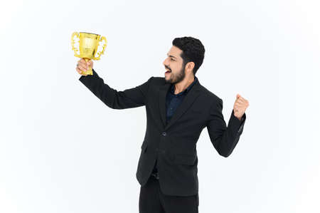 Portrait of Winning businessman celebrating with trophy award for success in business isolated on white background. Successful employee holds golden cup. Looking at the cameraの写真素材