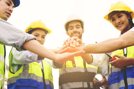 Group of contractors, engineers and formats in safety vests with helmets join hands to work together to successfully complete a construction project on construction site. cooperation and success conceptの写真素材