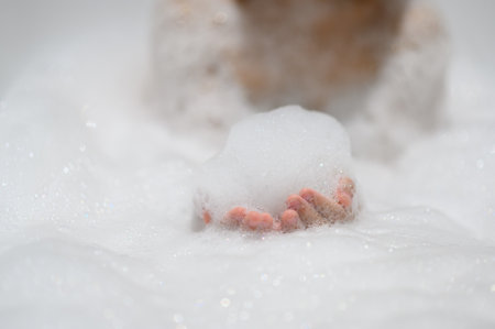 Close-up bubble foam on boy hands surrounded by soap suds when taking a bath in bathtub. Funny,...