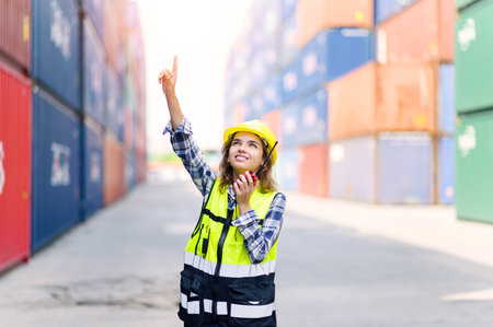 container operators women wearing helmets and safety vests control via walkie-talkie workers in container yards. Cargo Ship Import Export Factory Logistic.の写真素材