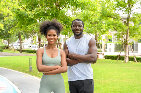 Portrait of Young African fitness couple in sportswear posing together and looking at camera while standing in public parkの写真素材