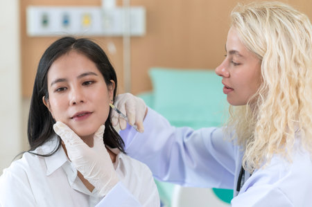 Woman doctor cosmetologist injects a filler into the cheek of the patient's woman. Cosmetology conceptの写真素材