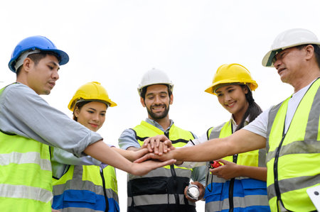 Group of contractors, engineers and formats in safety vests with helmets join hands to work together to successfully complete a construction project on construction site. cooperation and success conceptの写真素材