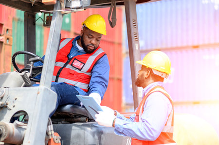 Two African American males in safety uniforms and helmets, container operating working with the forklift truck driver at commercial dock site. Cargo Ship Import Export Factory Logistic.の写真素材