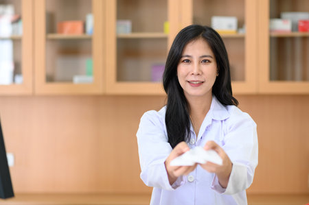 Smiling portrait of female pharmacist standing at the counter in pharmacy. Looking at cameraの写真素材