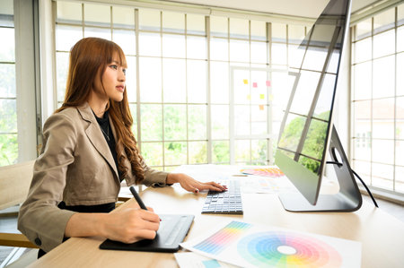 Asian female artist drawing something on graphic tablet. graphic designer working at officeの写真素材