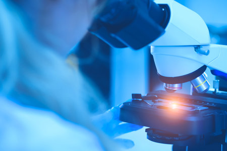 The scientist handed in blue gloves looking under a microscope to analyze the test sample. Medical...