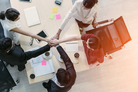Top view of business people clapping hands together over table, Below graphs placed on the desk. Young businessman and businesswoman stack of hands showing unity and teamwork support.の写真素材