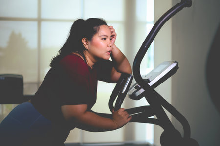 TiredÂ young Asian overweight women exercising on elliptical trainer in the gym. Weight loss...