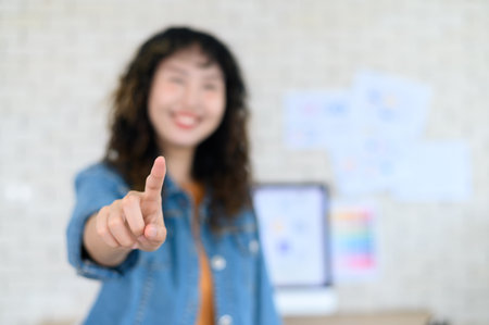 Happy blurred young woman graphic designer pointing finger at camera. Select focus to fingerの写真素材