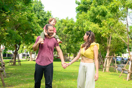 Happy Family. father, mother with little child in the park on a sunny summer day together. Son sitting on his father shoulders happy in vacation timeの写真素材