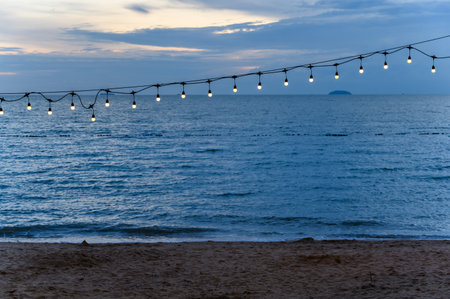 light bulbs on string wire decoration at the party event festival on the beach at sunset. Outdoor holiday background. Copy spaceの写真素材