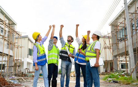 Group of contractors, engineers and formats in safety vests with helmets hands up to work together to successfully complete a construction project on construction site. cooperation and success conceptの写真素材