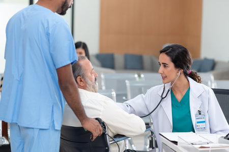 Old patient man sitting in wheelchair while young female doctor using stethoscope to check his heartbeat, elderly health checkup, happiness hospitalの写真素材