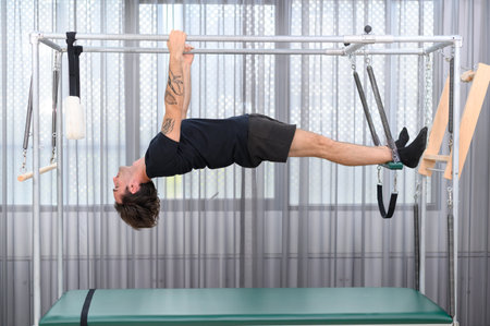 Sportsman doing pilates aerial exercise on a trapeze table for flexibility and core training in fitness studioの写真素材