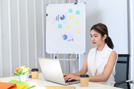 businesswoman sitting at the table while busy working on laptop computer at the office. Woman typing document, checking email, and participating in online meetings at workplaceの写真素材