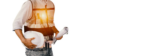 Portrait ofÂ young attractive construction man smiling bearded in vest and holding white helmet and blueprint while standing on construction site. Home building conceptの写真素材