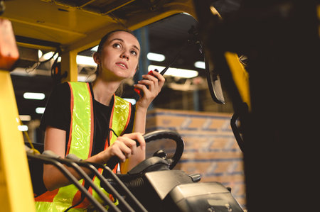 warehouse, radio, and forklift in shipping warehouse. Female transport worker in safety uniform transport worker talking on walkie talkie, drives forklift at freight cargo warehouse portの写真素材