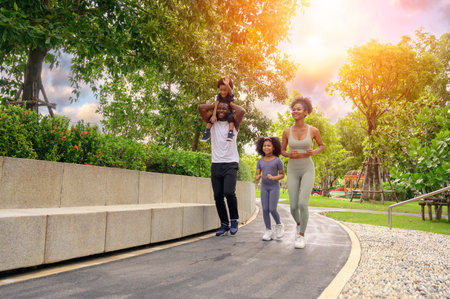 Happy African American family in sportswear running in public park. father carrying son with mother and daughter. Family exercising together conceptの写真素材