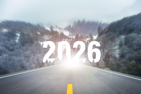 Empty asphalt road leading into snowy forest mountains with large glowing number 2026 at the...
